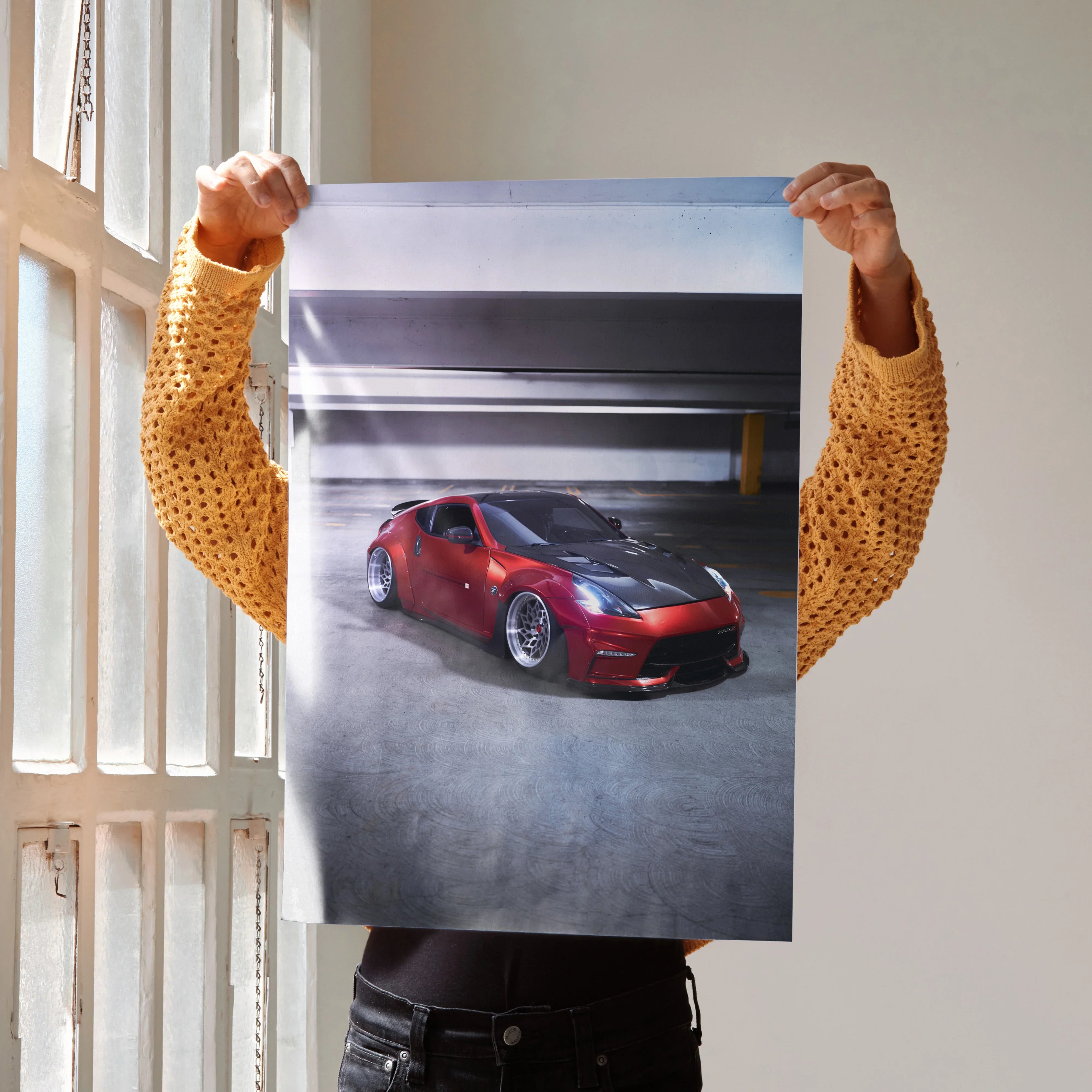 Nissan 370Z poster wall art held up indoors featuring red sports car in urban parking garage setting.