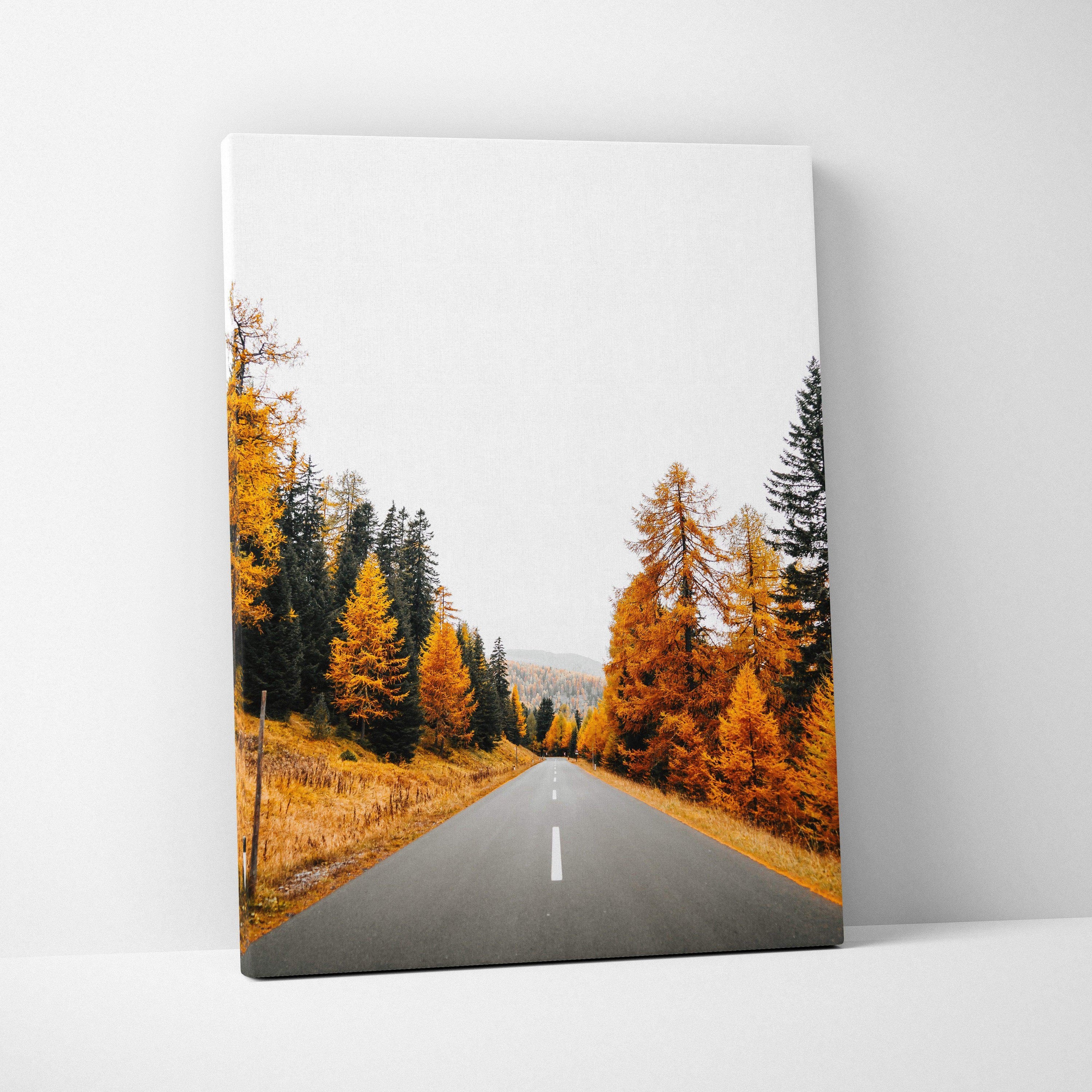 Vertical canvas wall art featuring a road through vibrant autumn trees with orange leaves.