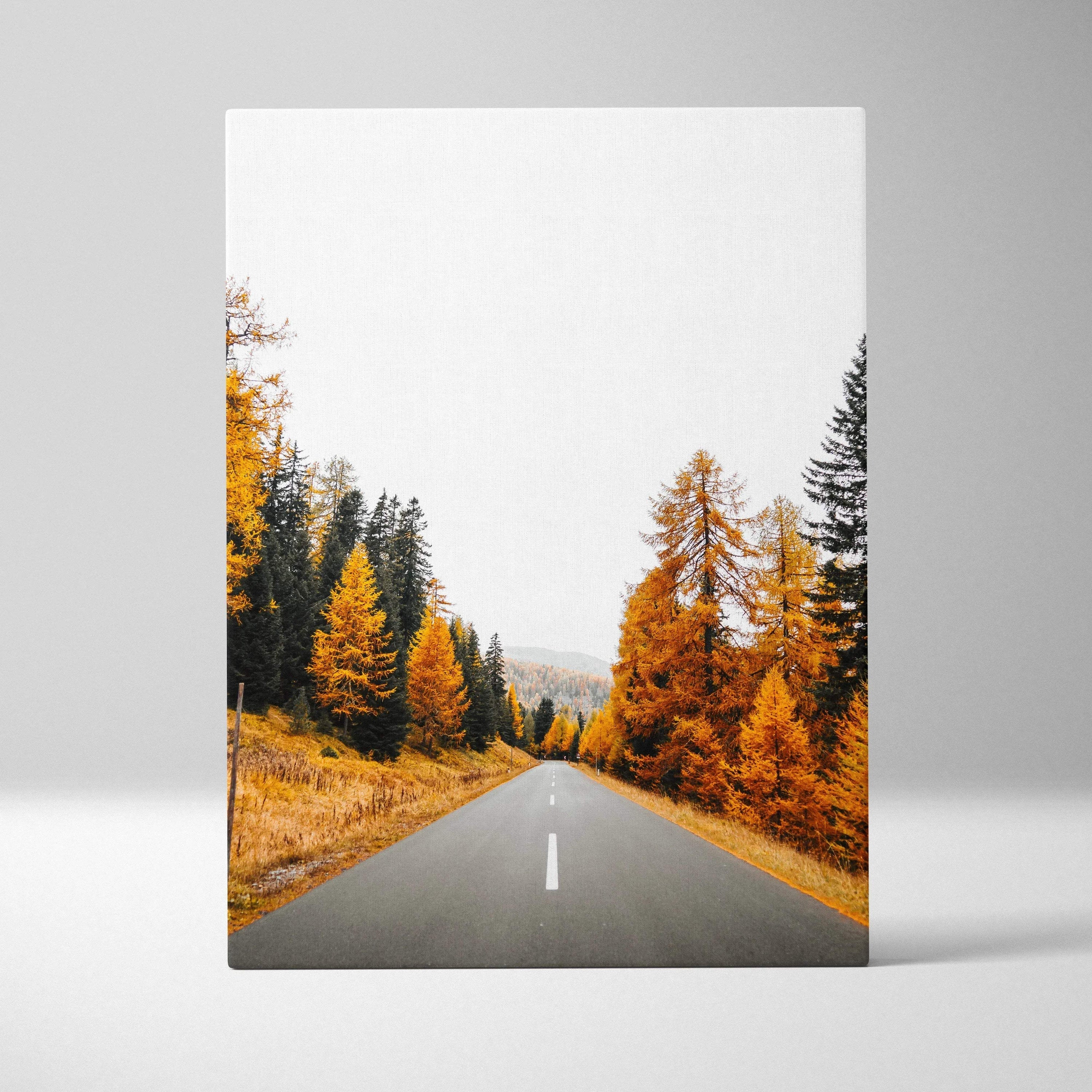 Vertical canvas wall art featuring a vibrant autumn landscape with orange and yellow trees along a road.