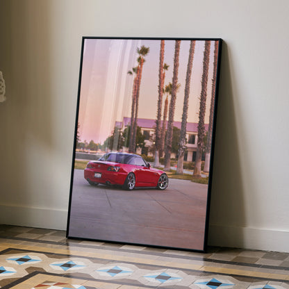 Red Honda S2000 parked by palm trees at sunset poster wall art in black frame.
