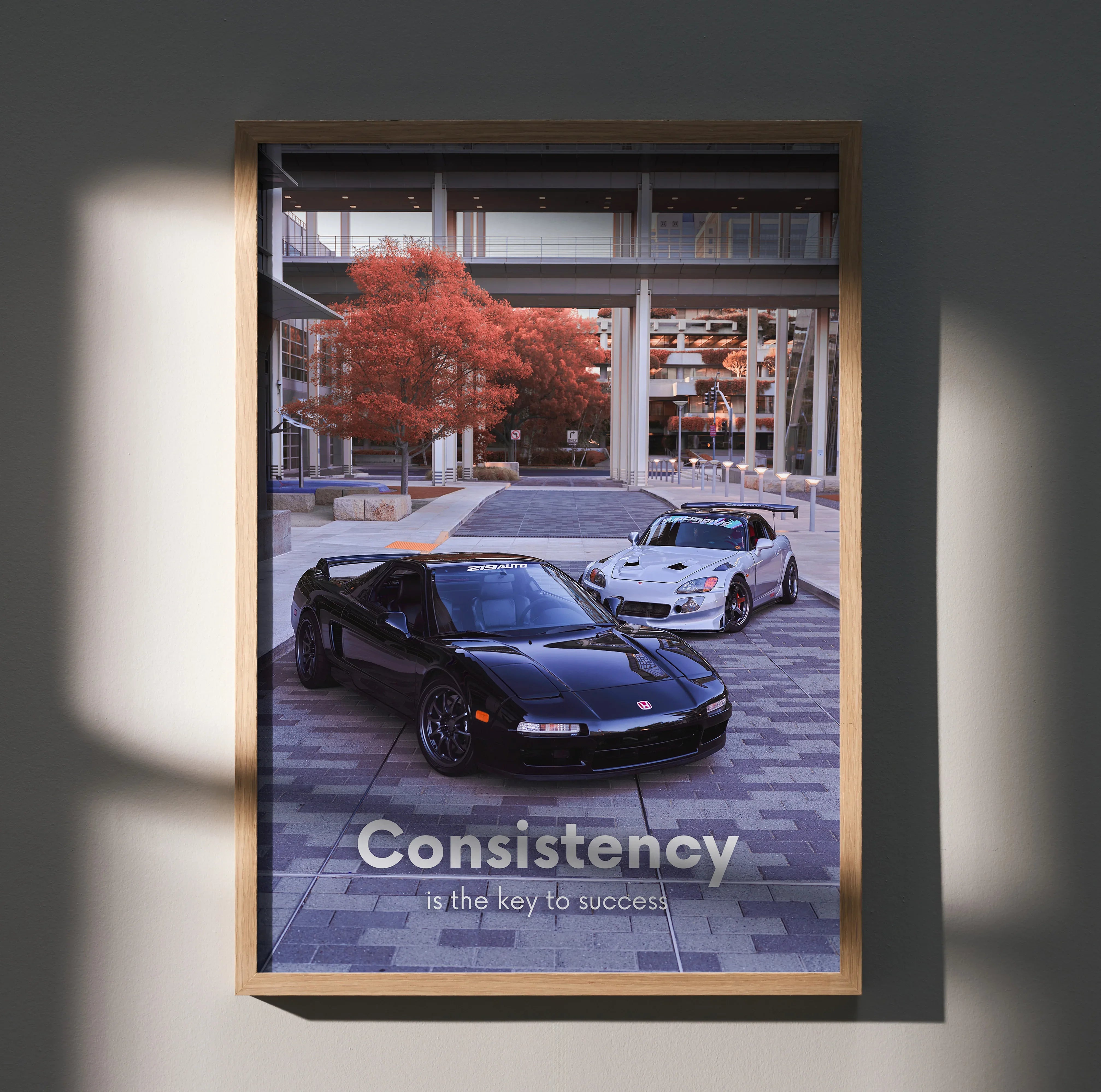 Motivational poster wall art featuring black Acura NSX and white Honda S2000 under modern bridge with red tree.