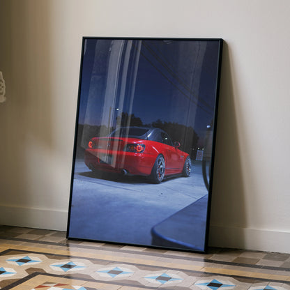 Red Honda S2000 sports car poster leaning against wall, glossy wall art in black frame.