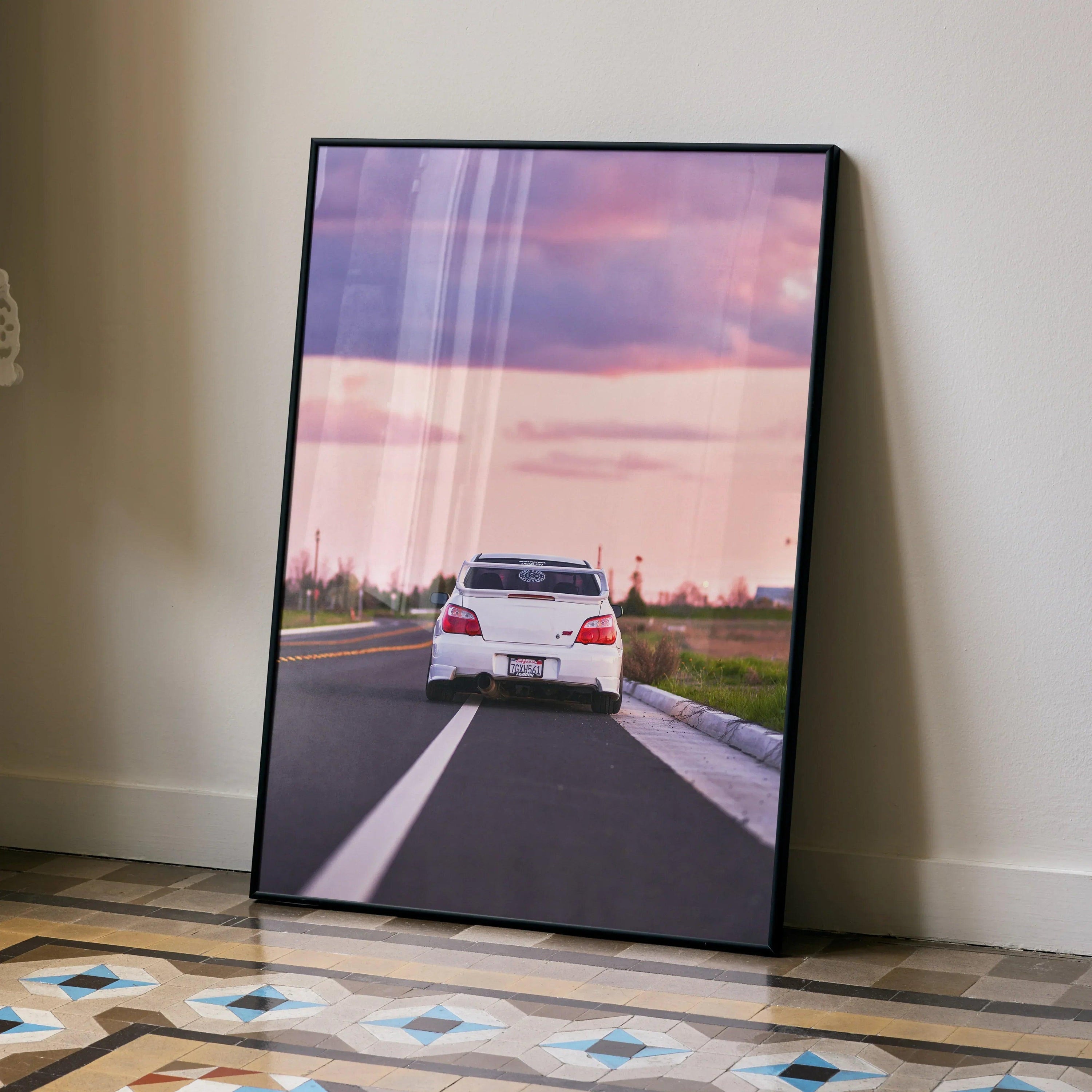 Subaru WRX STI speeding on road at sunset poster wall art in black frame on floor.