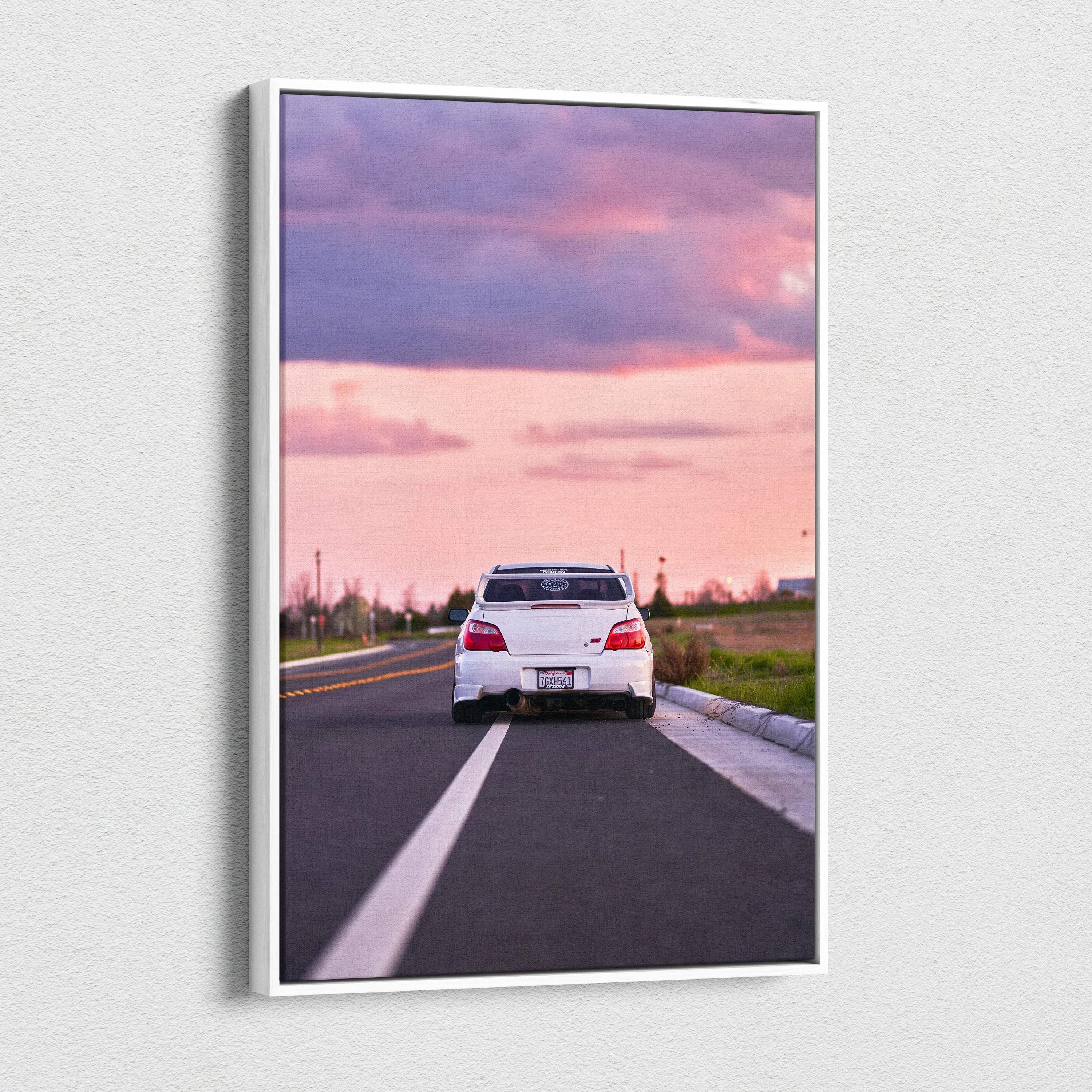 Vertical canvas wall art of a white Subaru WRX STI on a road at sunset with pink and purple sky.