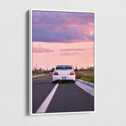 Vertical canvas wall art of a white Subaru WRX STI on a road at sunset with pink and purple sky.