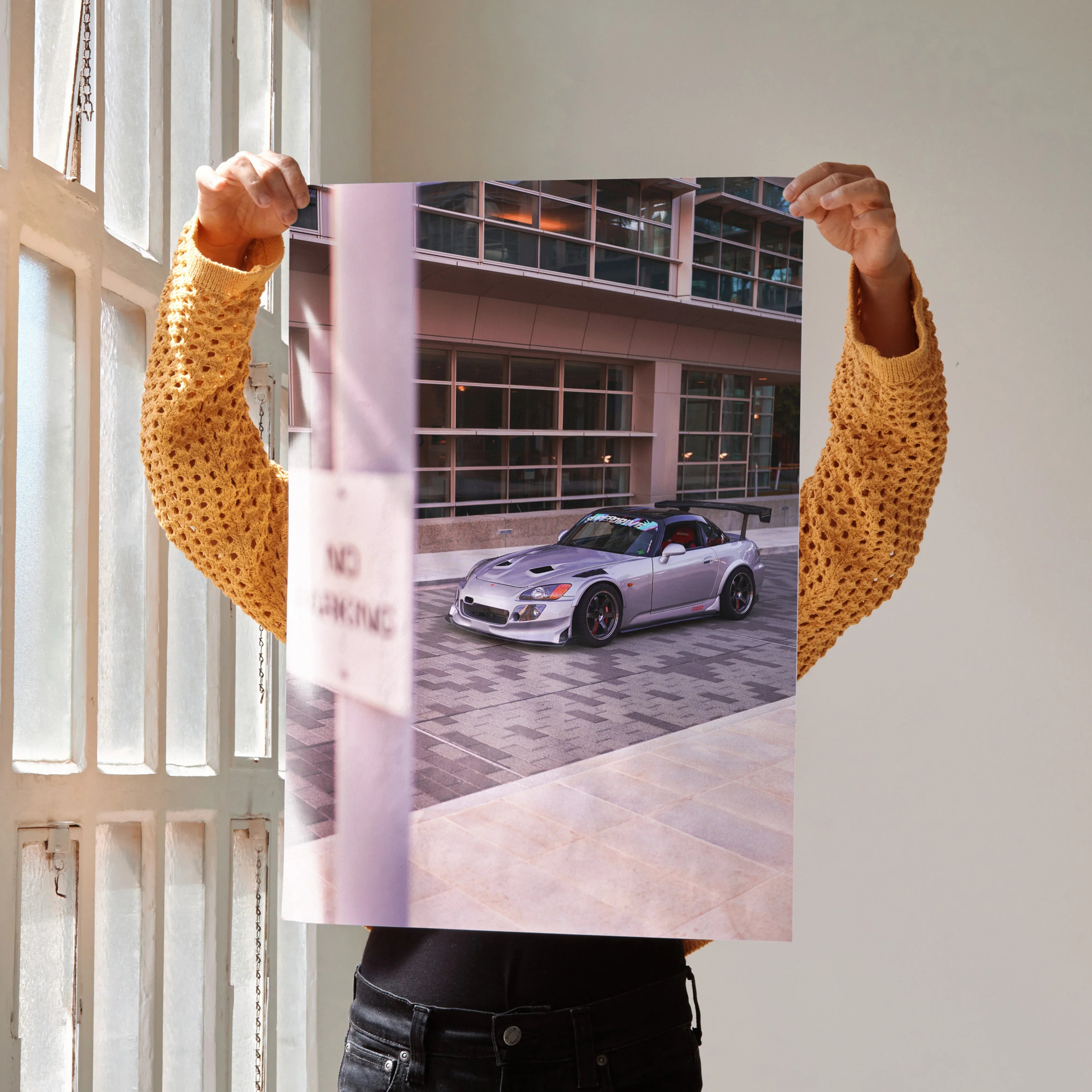 Honda S2000 poster wall art held up in bright natural light near window with modern building background.