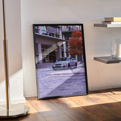 Nissan GTR R34 Skyline poster with urban background in black frame wall art resting on wooden floor.