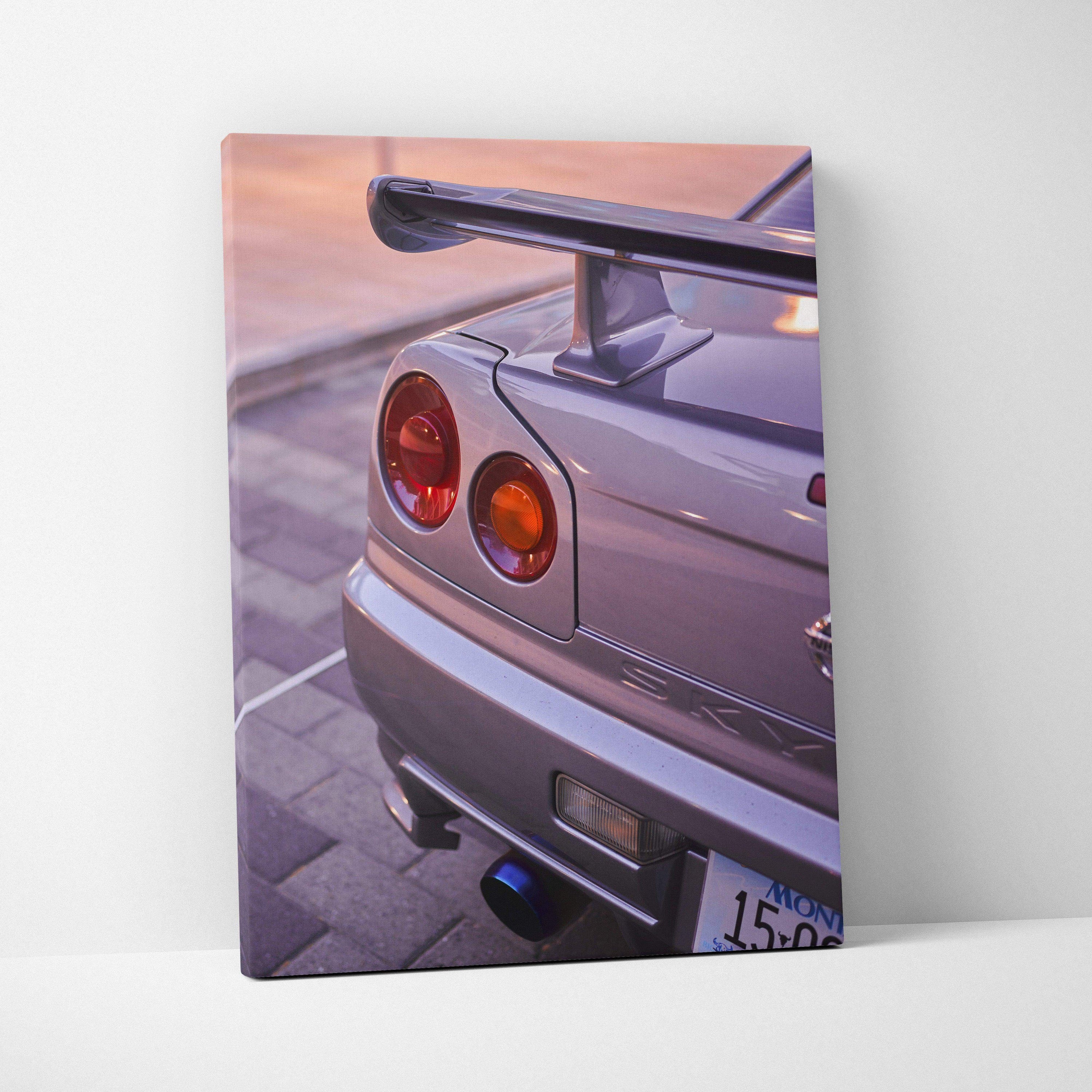 Vertical canvas wall art featuring the rear view of a silver Nissan GTR R34 Skyline at sunset.