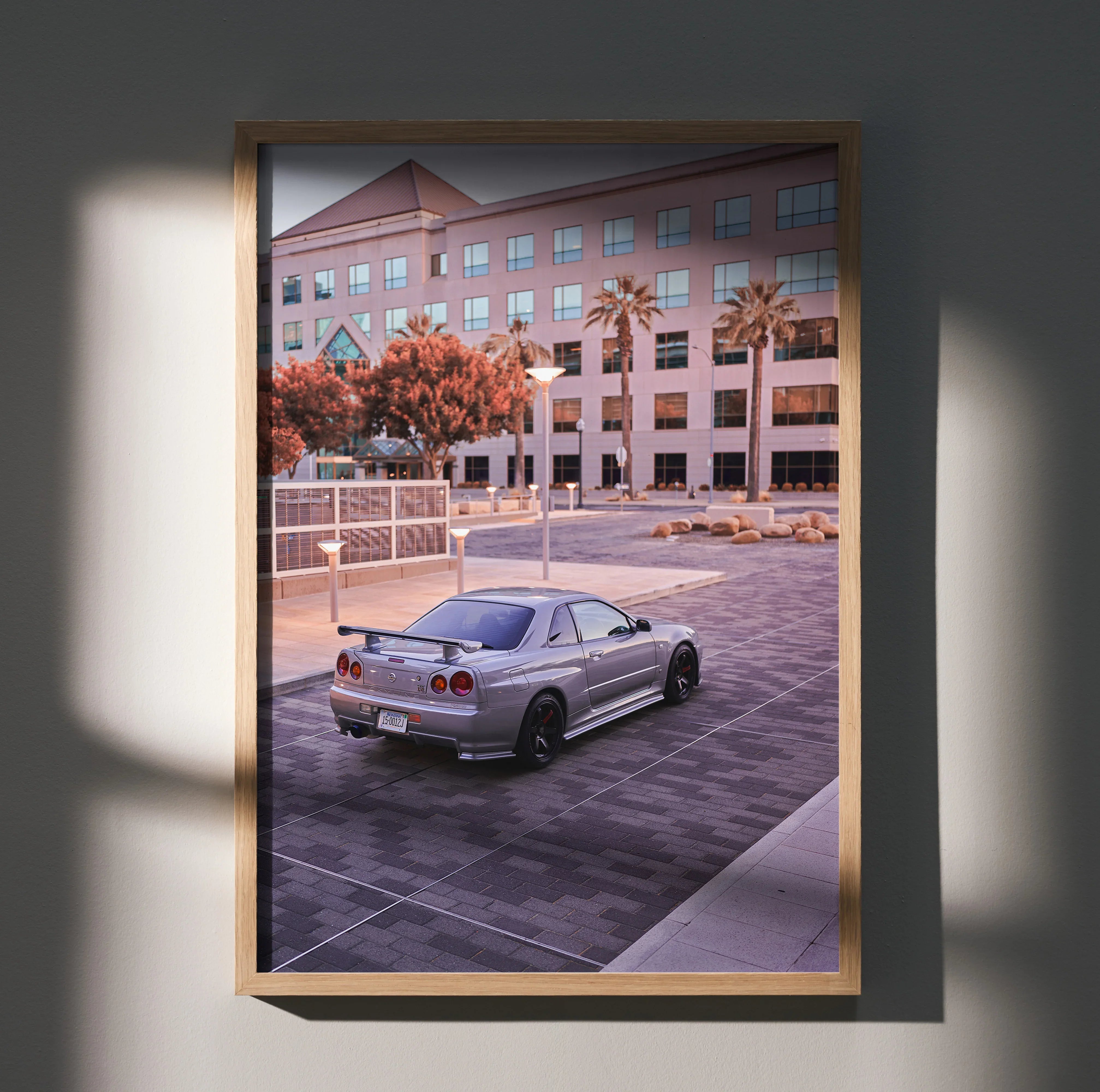 Nissan R34 GTR Skyline parked in urban setting poster wall art with warm tones and modern building backdrop.