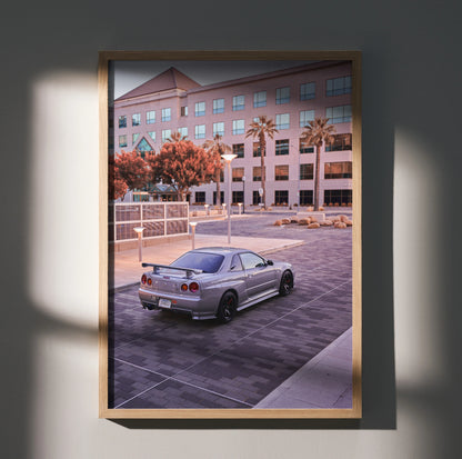 Nissan R34 GTR Skyline parked in urban setting poster wall art with warm tones and modern building backdrop.