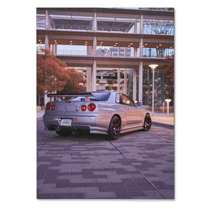 Nissan R34 GTR Skyline poster showing rear view with urban backdrop, sleek silver car, and modern architecture wall art.