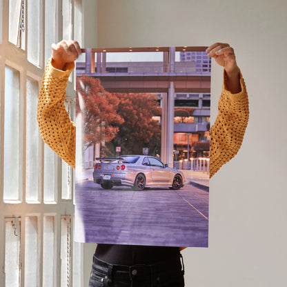 Nissan GTR R34 Skyline poster wall art featuring the car parked with city buildings in the background.