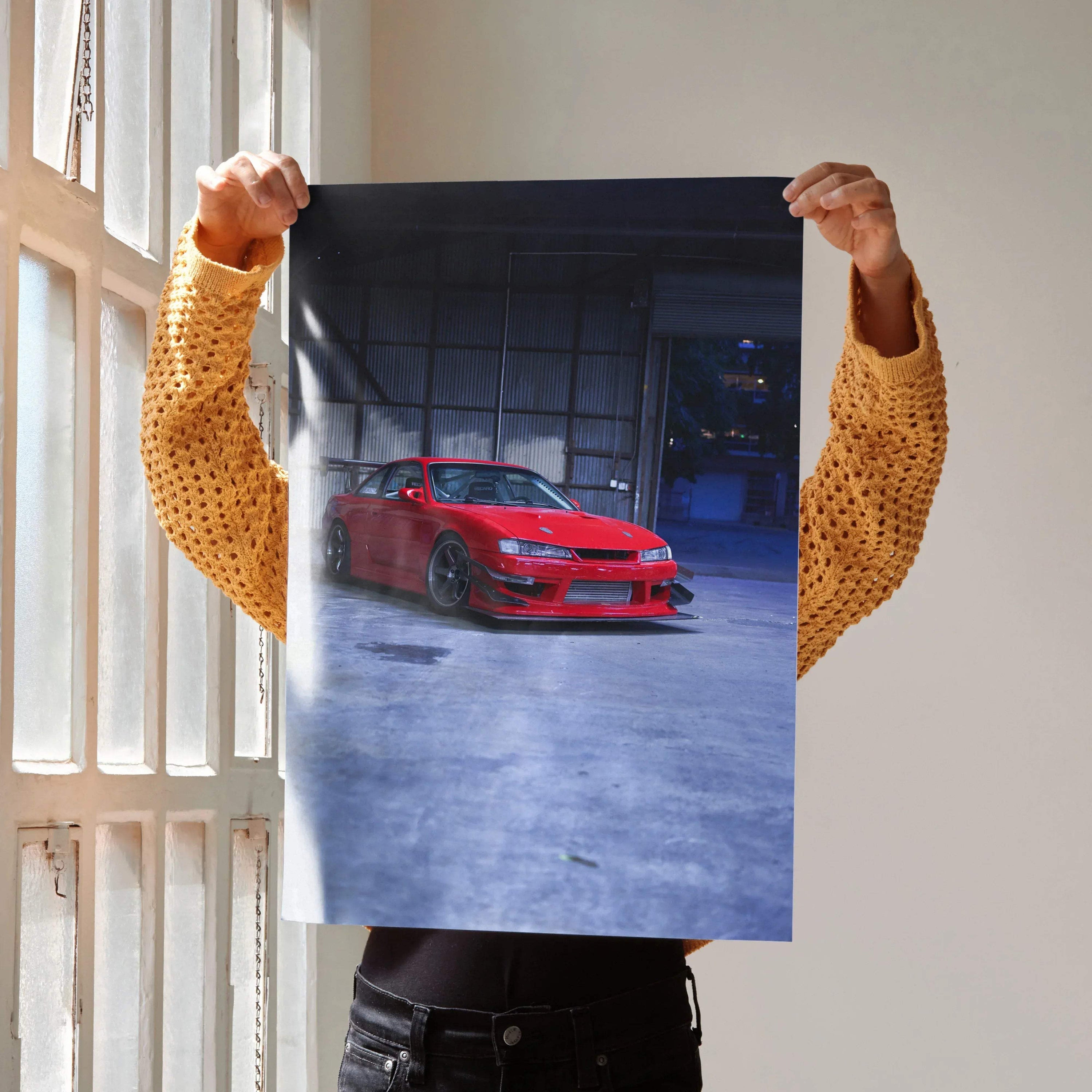 Red Nissan 240sx S14 Kouki car poster wall art held indoors with industrial background.