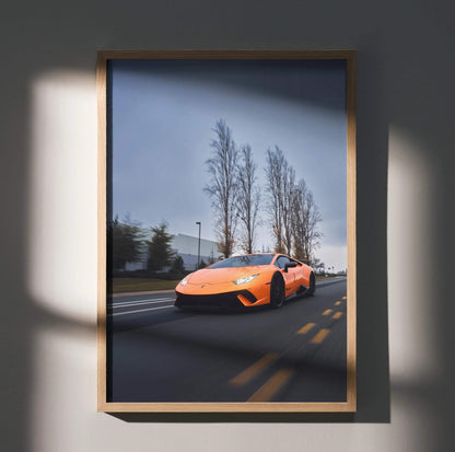 Orange Lamborghini Huracan driving on road with bare trees, premium wall art poster in wooden frame.