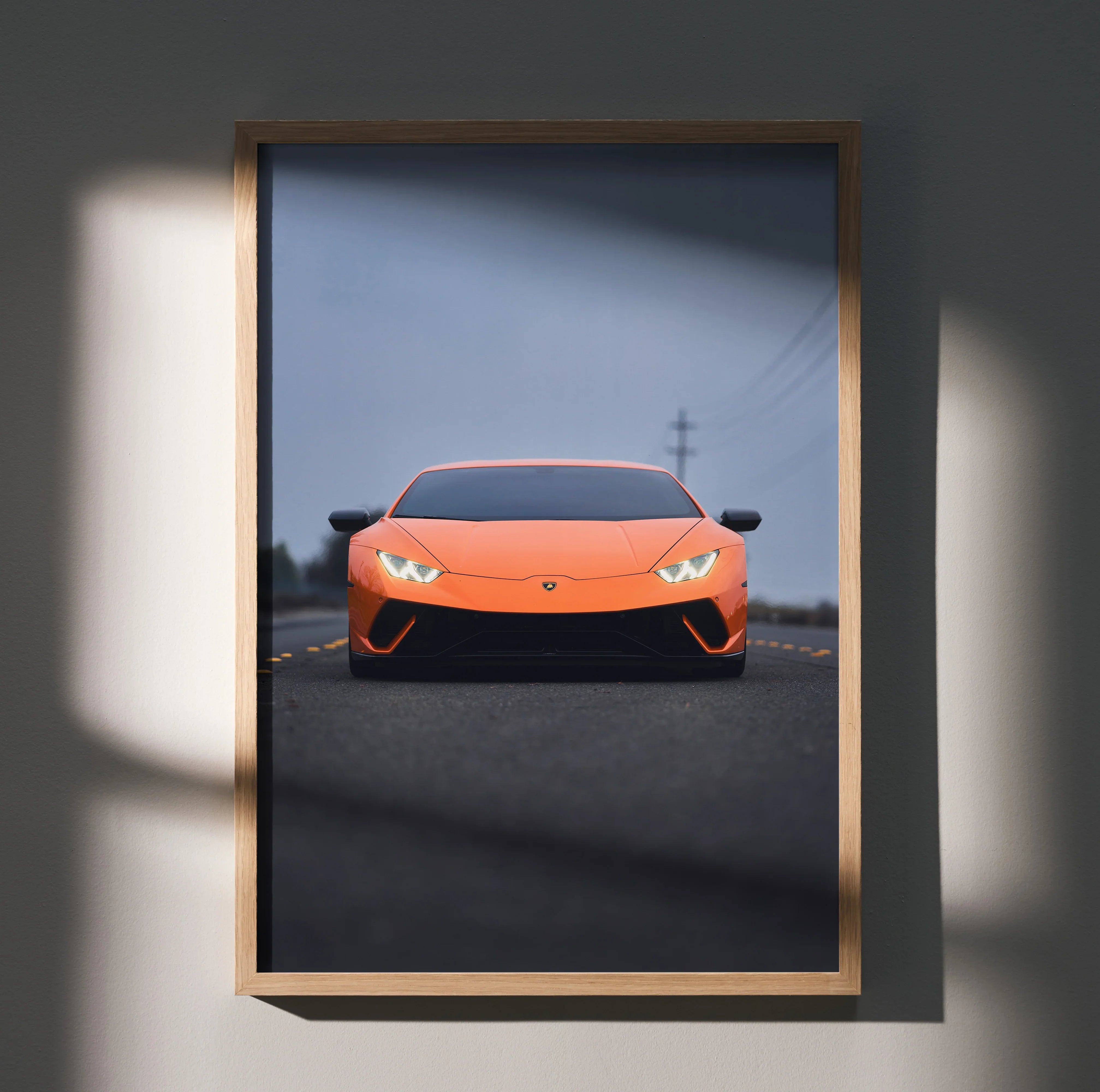 Orange Lamborghini Huracan poster with sleek front view on dark road, framed wall art with shadow detail.
