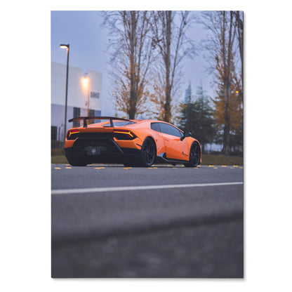 Orange Lamborghini Huracan parked outdoors at dusk with trees and streetlights, automotive poster wall art.
