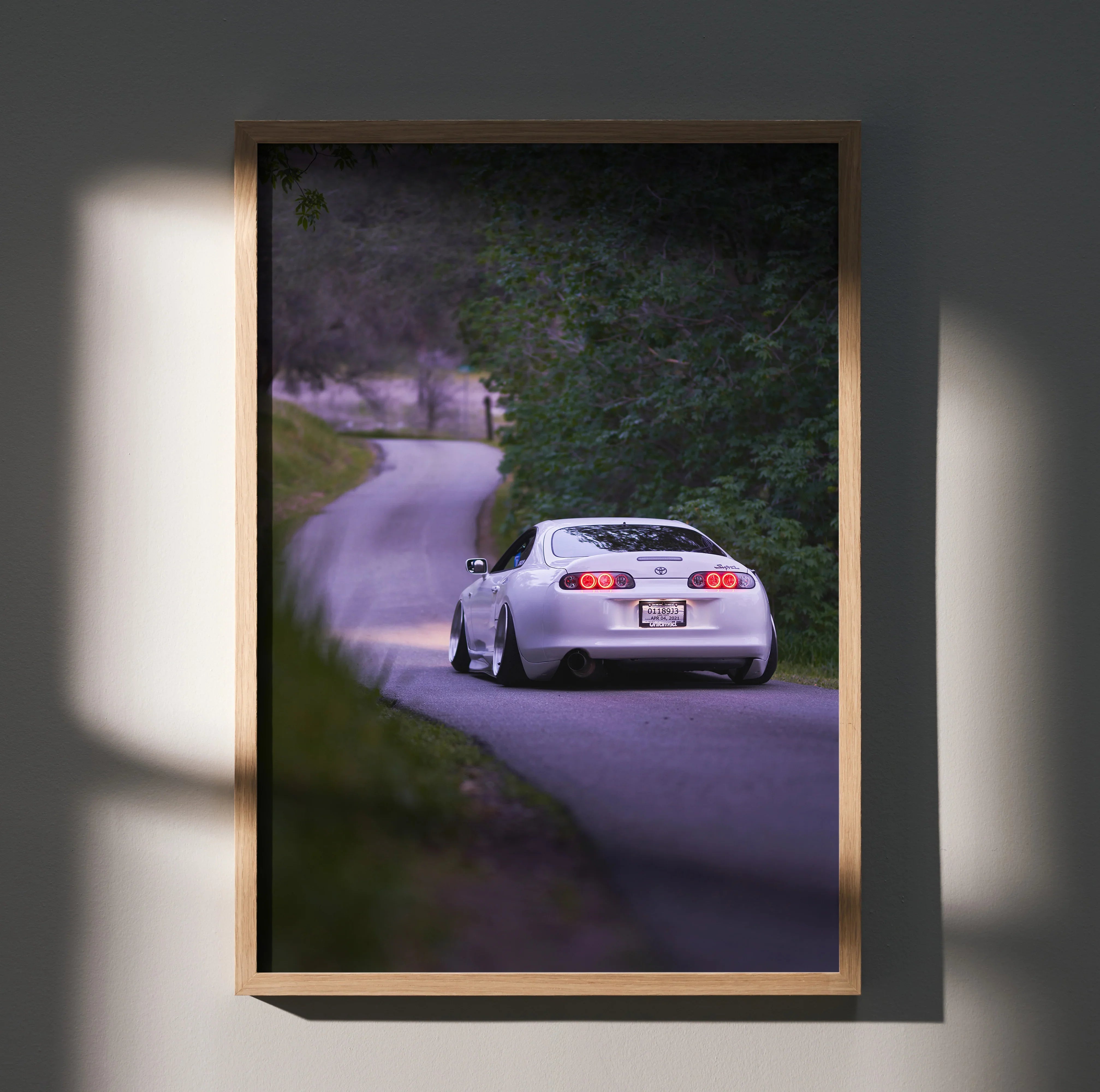 Toyota Supra MK4 driving on winding road poster with natural greenery wall art in wooden frame.