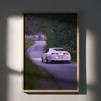 Toyota Supra MK4 driving on winding road poster with natural greenery wall art in wooden frame.