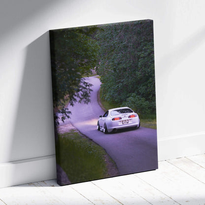 Toyota Supra MK4 driving on winding road canvas wall art with lush green trees.