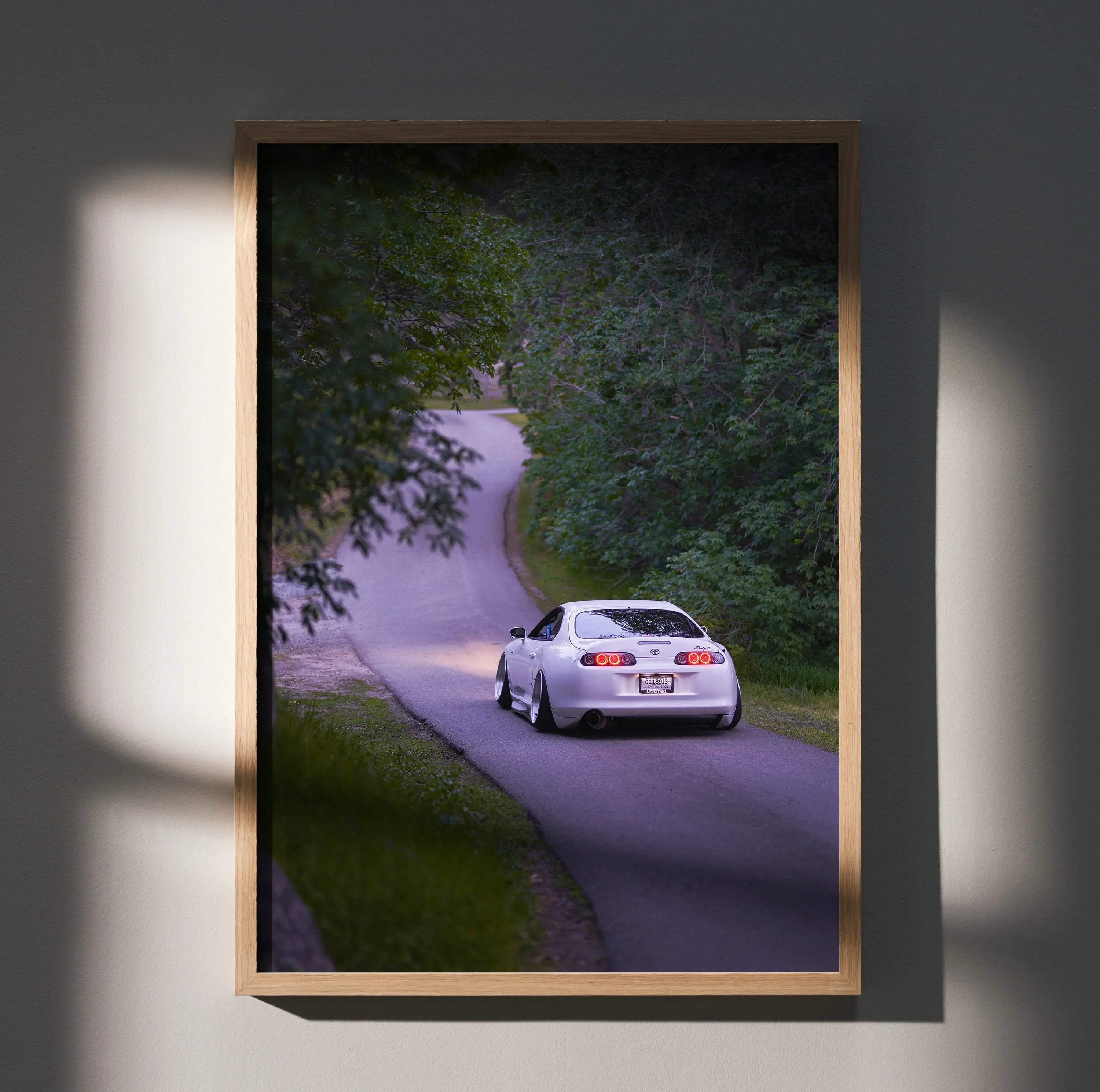 Toyota Supra MK4 driving on winding road wall art poster with lush green trees.