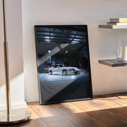 Toyota Supra MK4 poster wall art in black frame leaning against white wall on wooden floor.