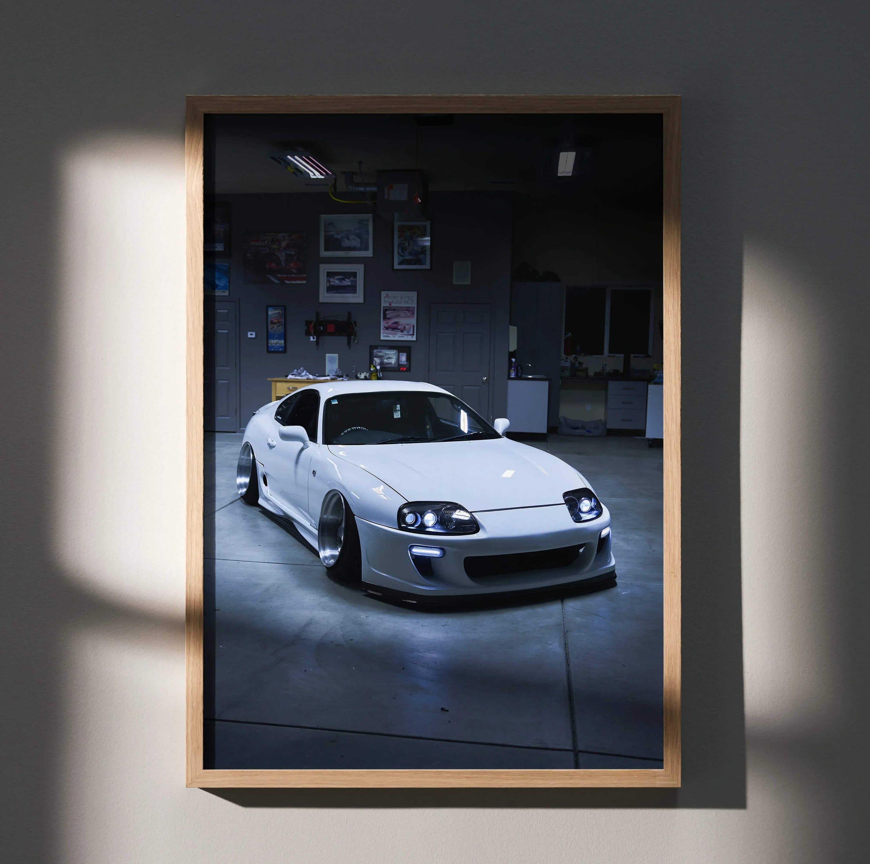 Toyota Supra MK4 in white sleek design poster wall art with dark garage background and wooden frame.
