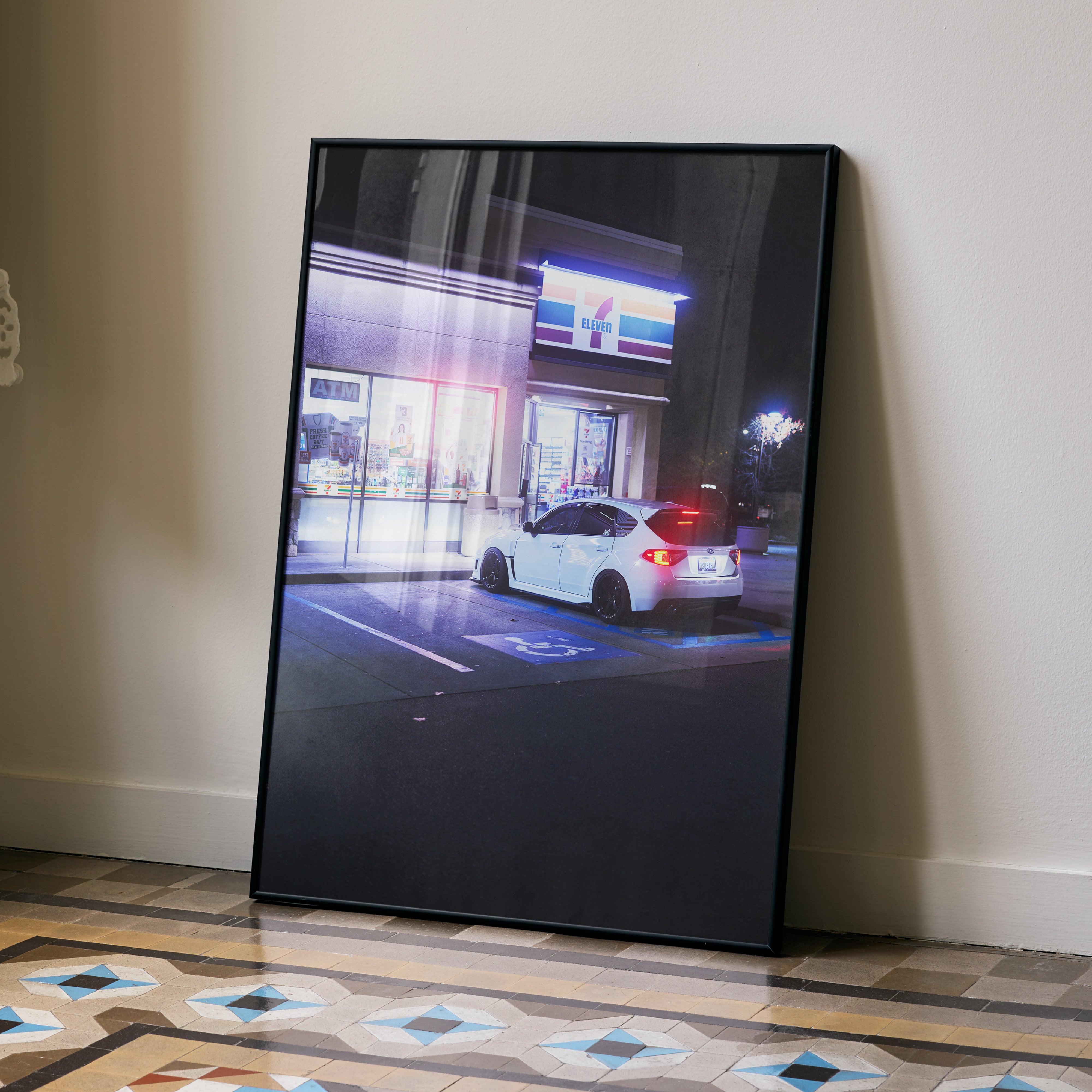 Framed Subaru WRX STI poster wall art leaning against wall with night cityscape and car in parking lot.