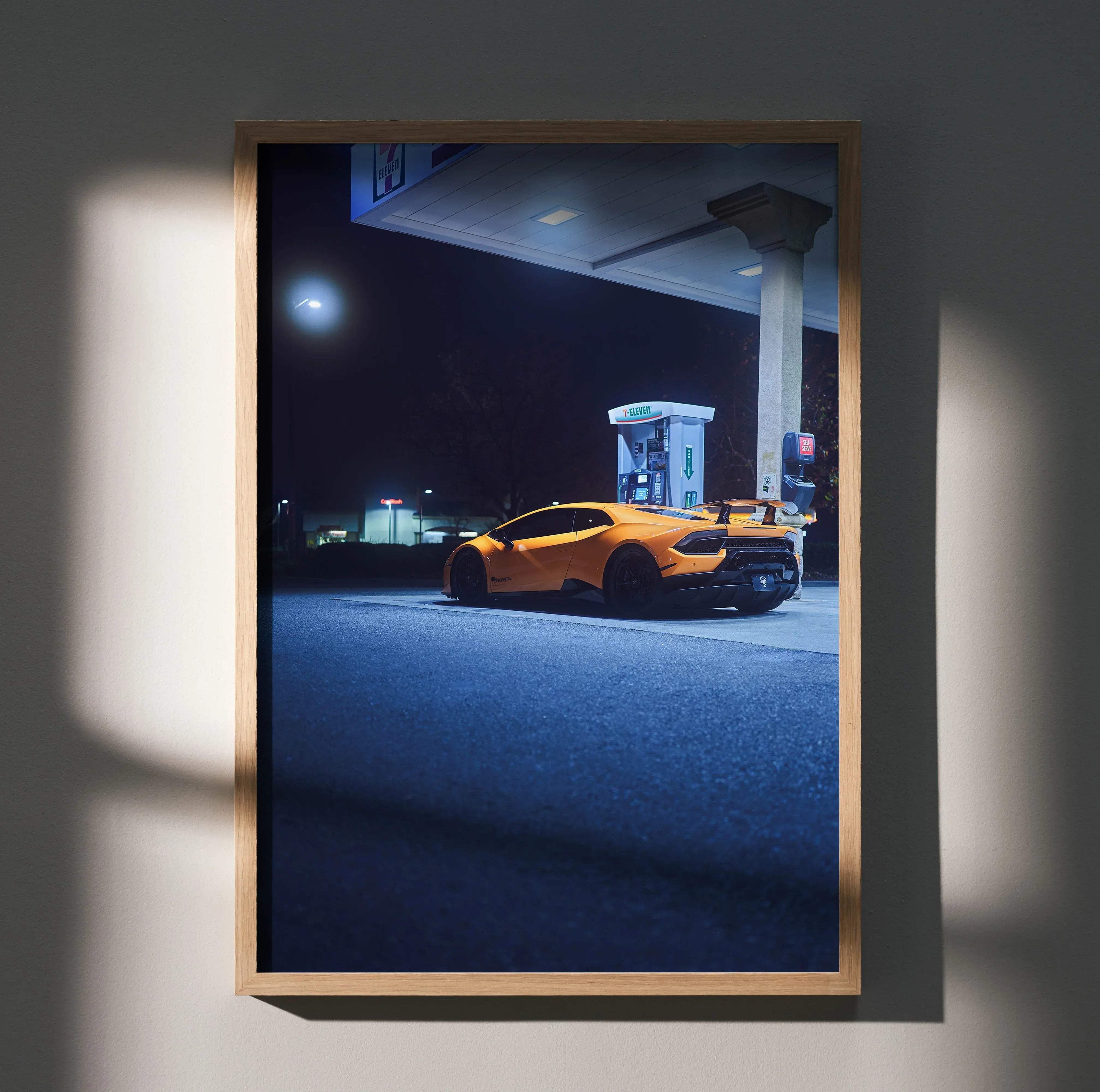 A framed vibrant orange Lamborghini Huracan art poster displayed with nighttime gas station lighting