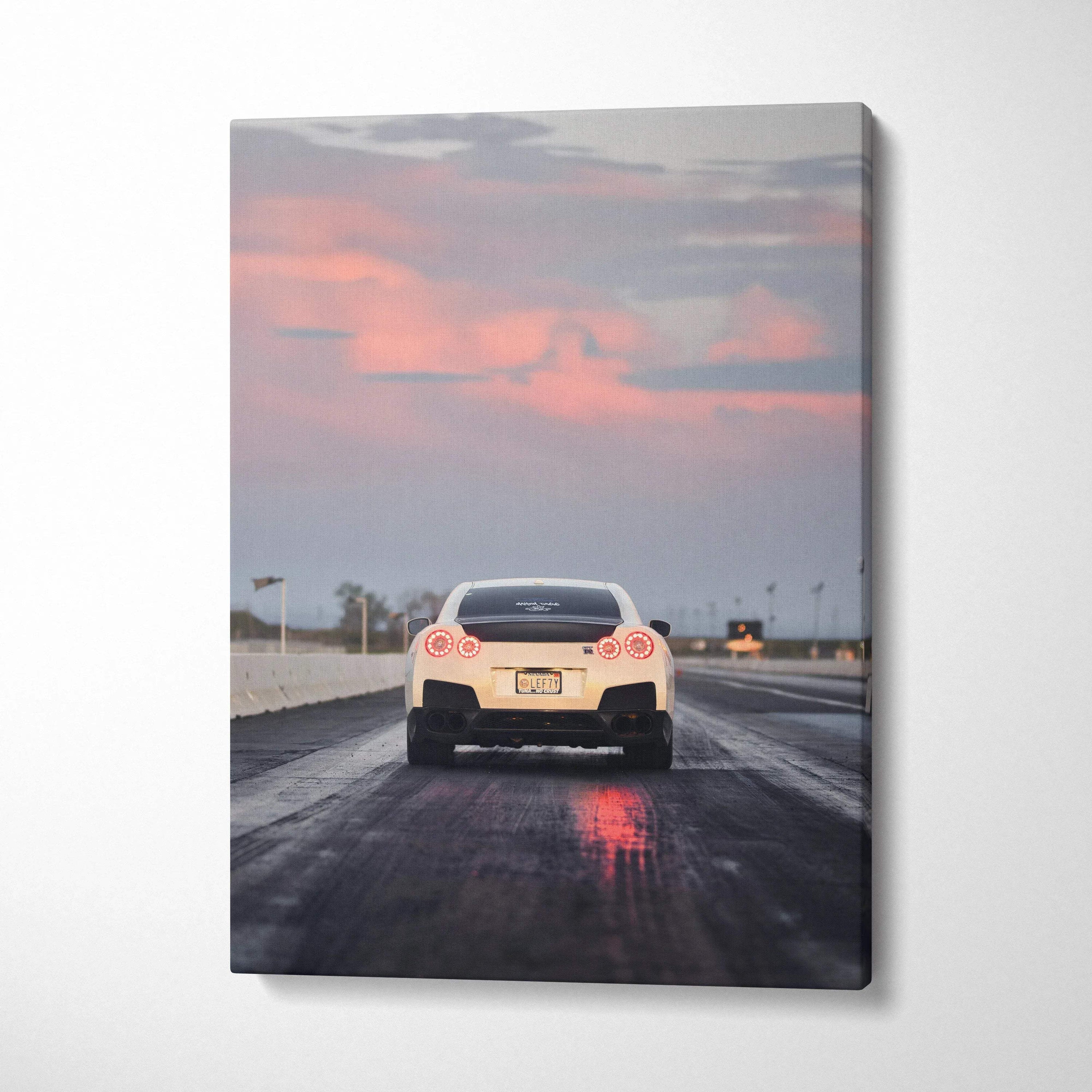 Vertical canvas wall art featuring rear view of white Nissan R35 GTR on wet road at sunset.