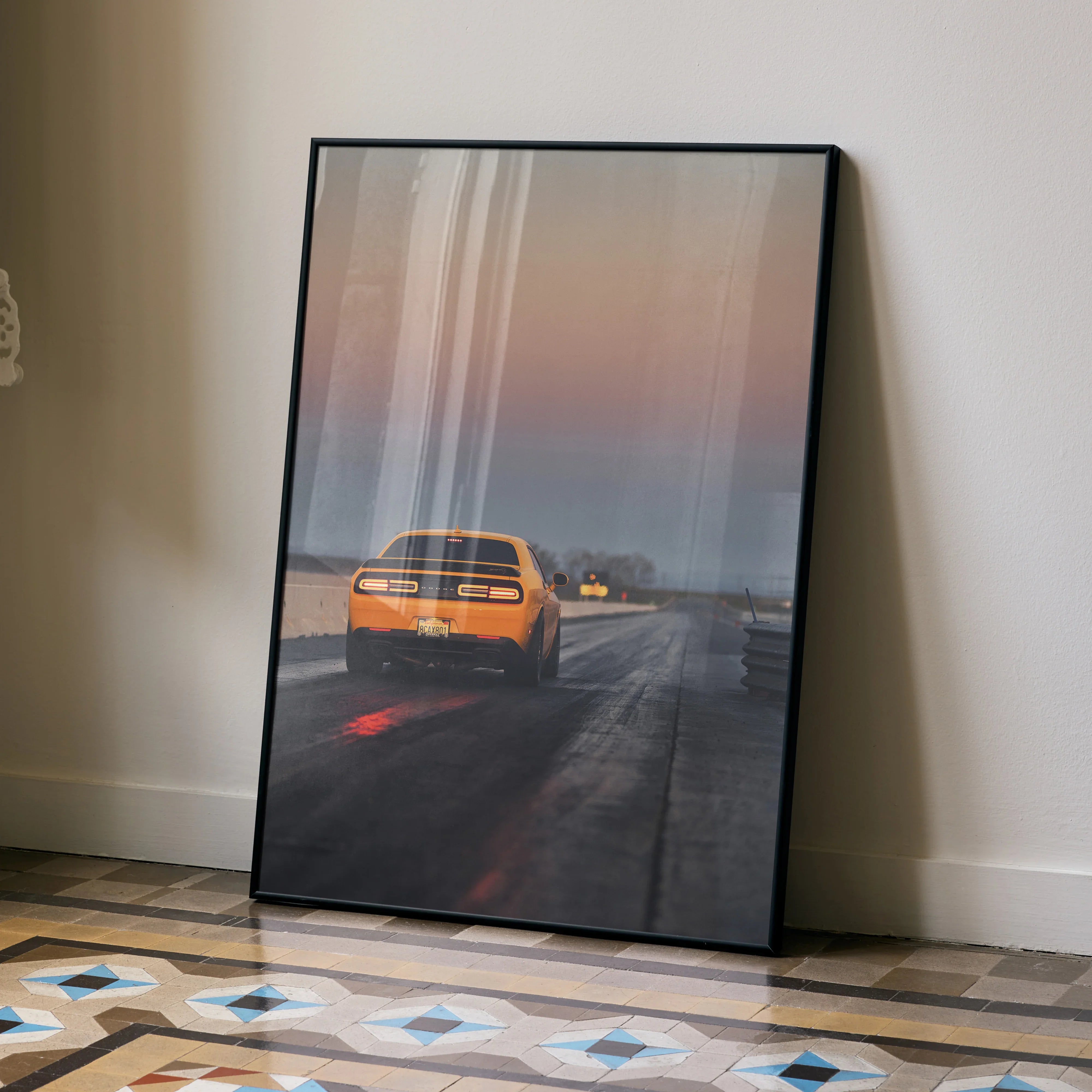 Dodge Challenger driving on road at sunset poster wall art in sleek black frame.