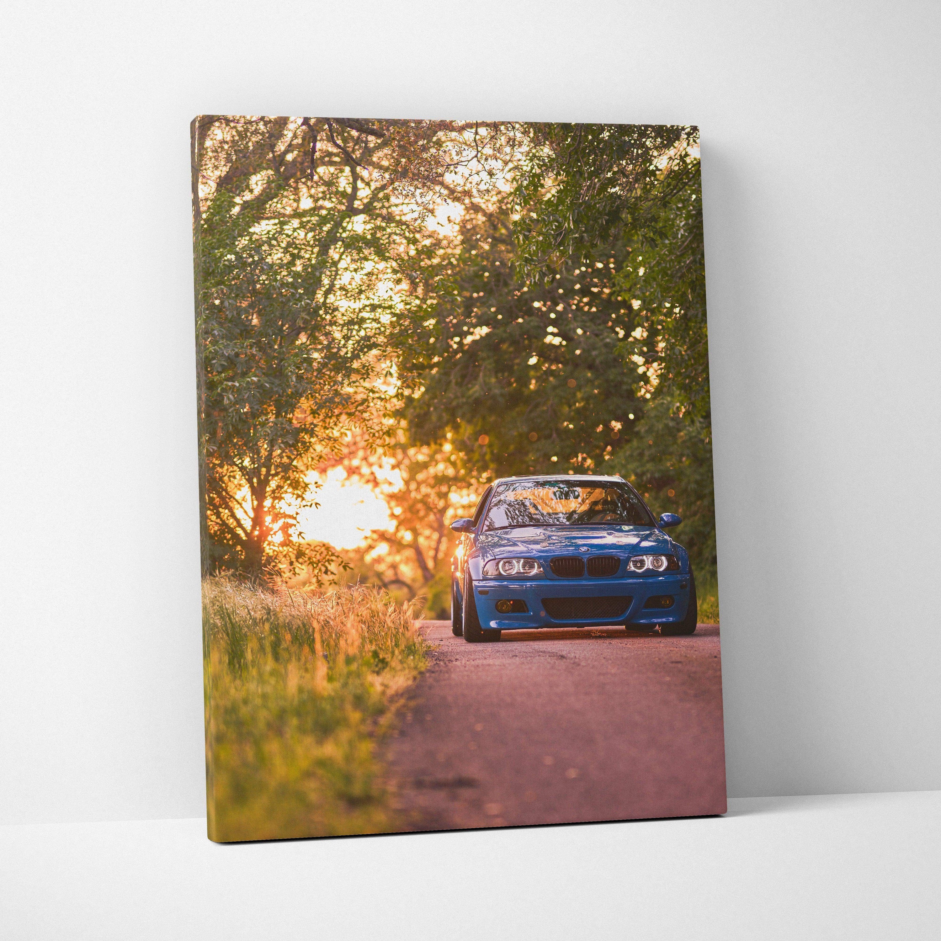 Vertical canvas wall art featuring a blue BMW E46 M3 on a road at sunset with trees and warm light.