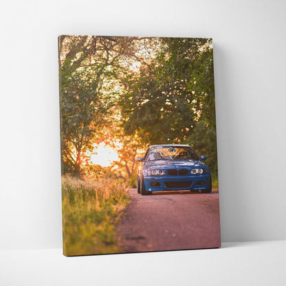 Vertical canvas wall art featuring a blue BMW E46 M3 on a road at sunset with trees and warm light.