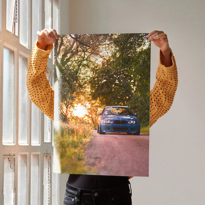 BMW E46 M3 poster featuring blue car on sunset road surrounded by trees, wall art for enthusiasts.