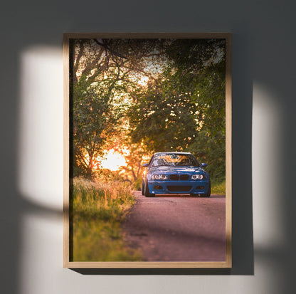 BMW E46 M3 driving on forest road at sunset poster wall art with warm light and shadows.
