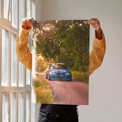 Poster of blue BMW E46 M3 driving on a scenic tree-lined road for automotive wall art.