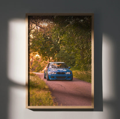 BMW E46 M3 driving on forest road at sunset poster wall art with warm lighting and wooden frame.
