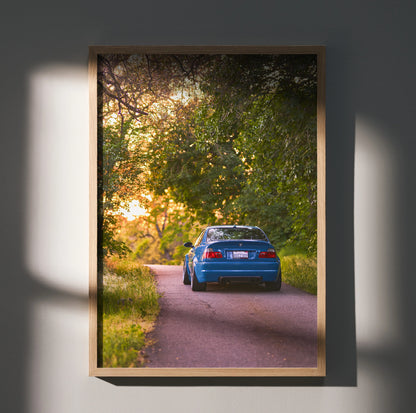 BMW E46 M3 driving on a scenic tree-lined road at sunset poster wall art.