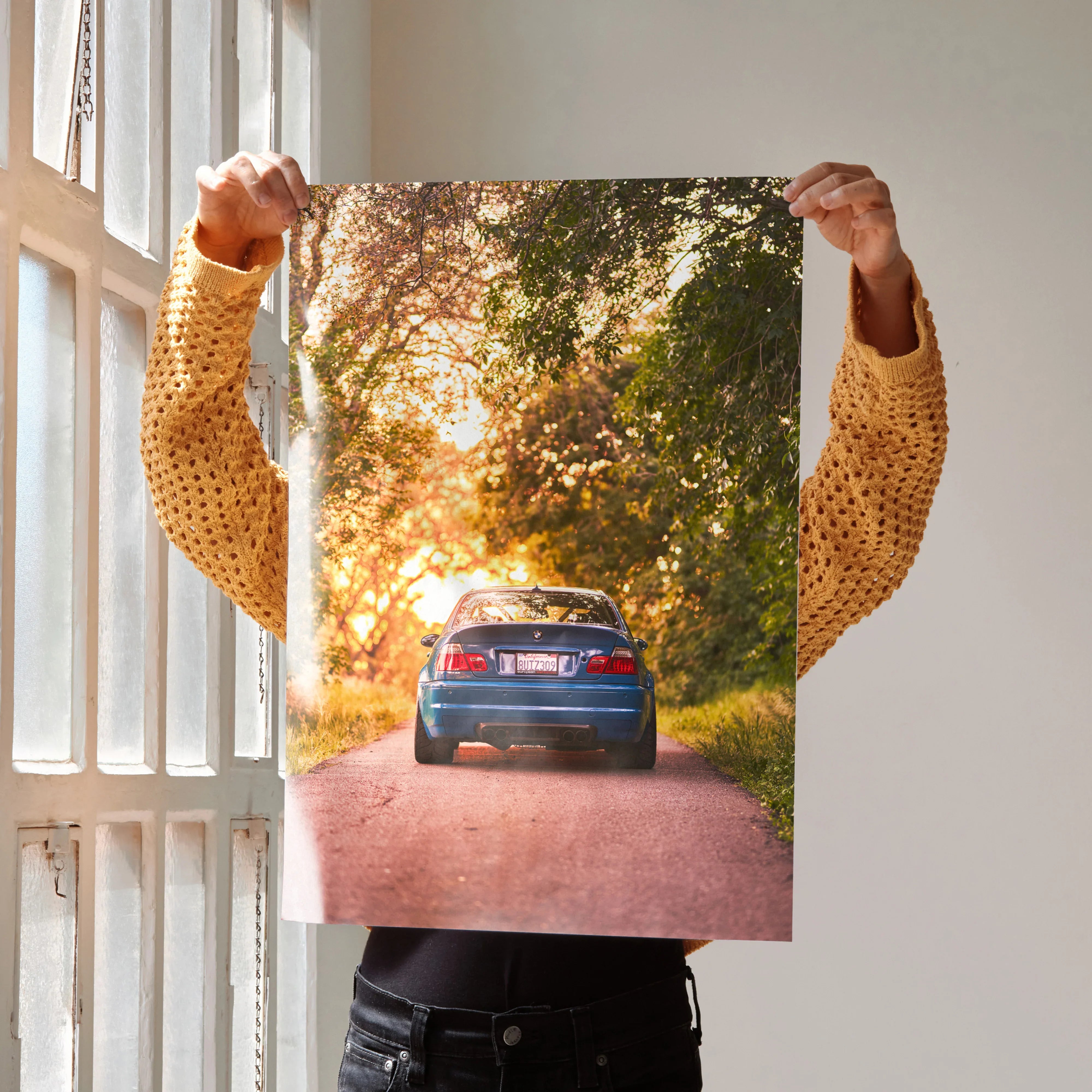 Blue BMW E46 M3 car on sunlit forest road poster wall art with warm sunset tones.