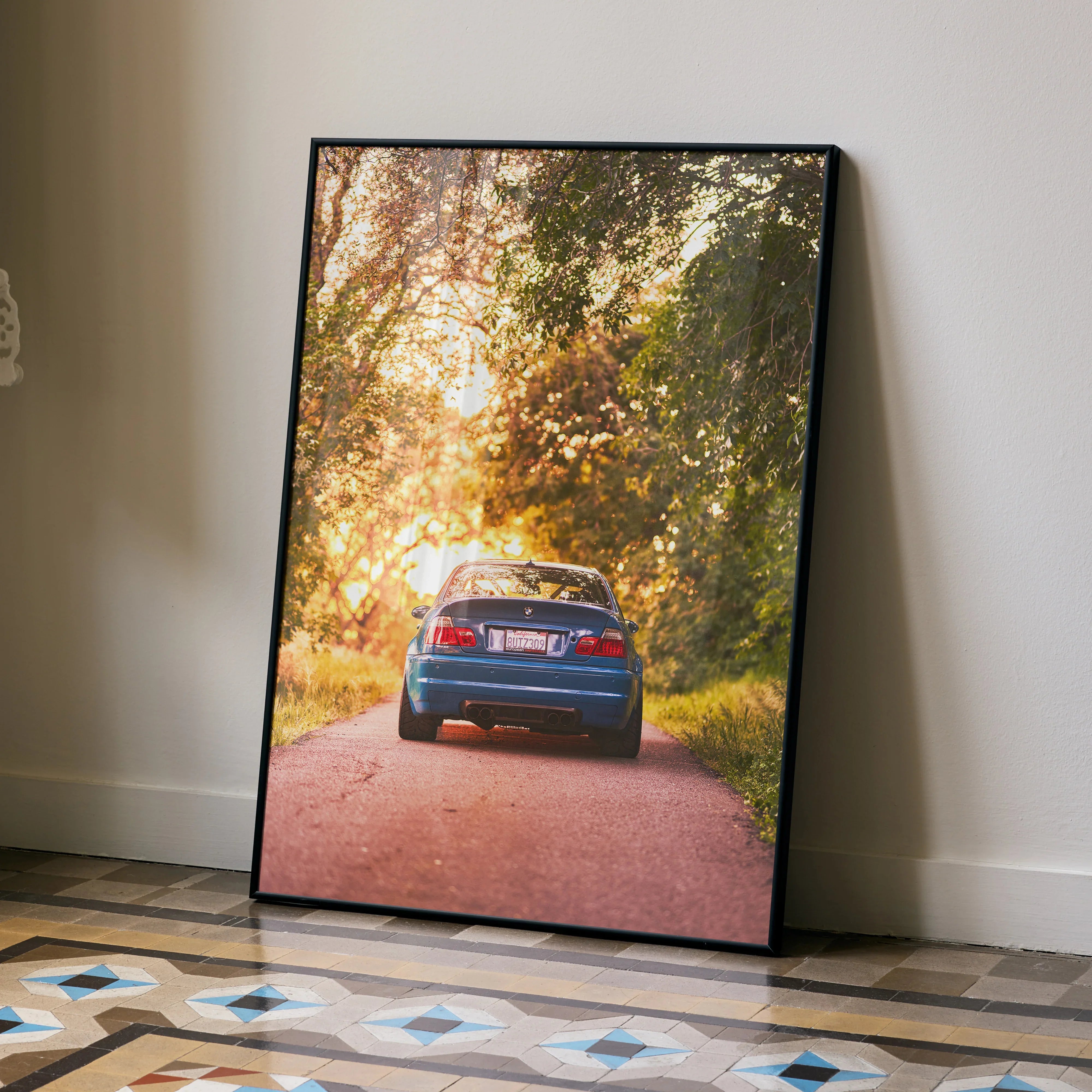 BMW E46 M3 car poster on floor with autumn trees and sunset wall art in black frame.