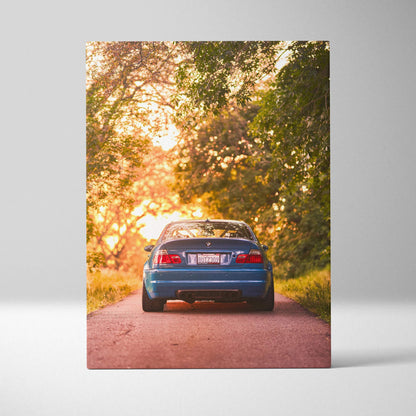 Blue BMW E46 M3 on sunset road surrounded by trees vertical canvas wall art.