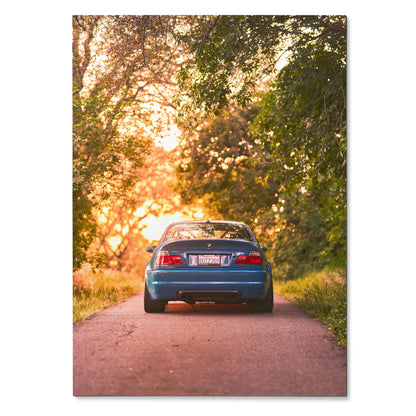 Blue BMW E46 M3 on sunset road surrounded by trees, high-resolution poster wall art.