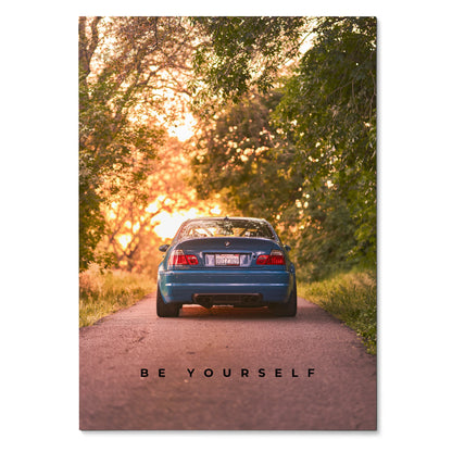 Motivational poster wall art featuring rear view of blue BMW E46 M3 on tree-lined road at sunset with "Be Yourself" text.