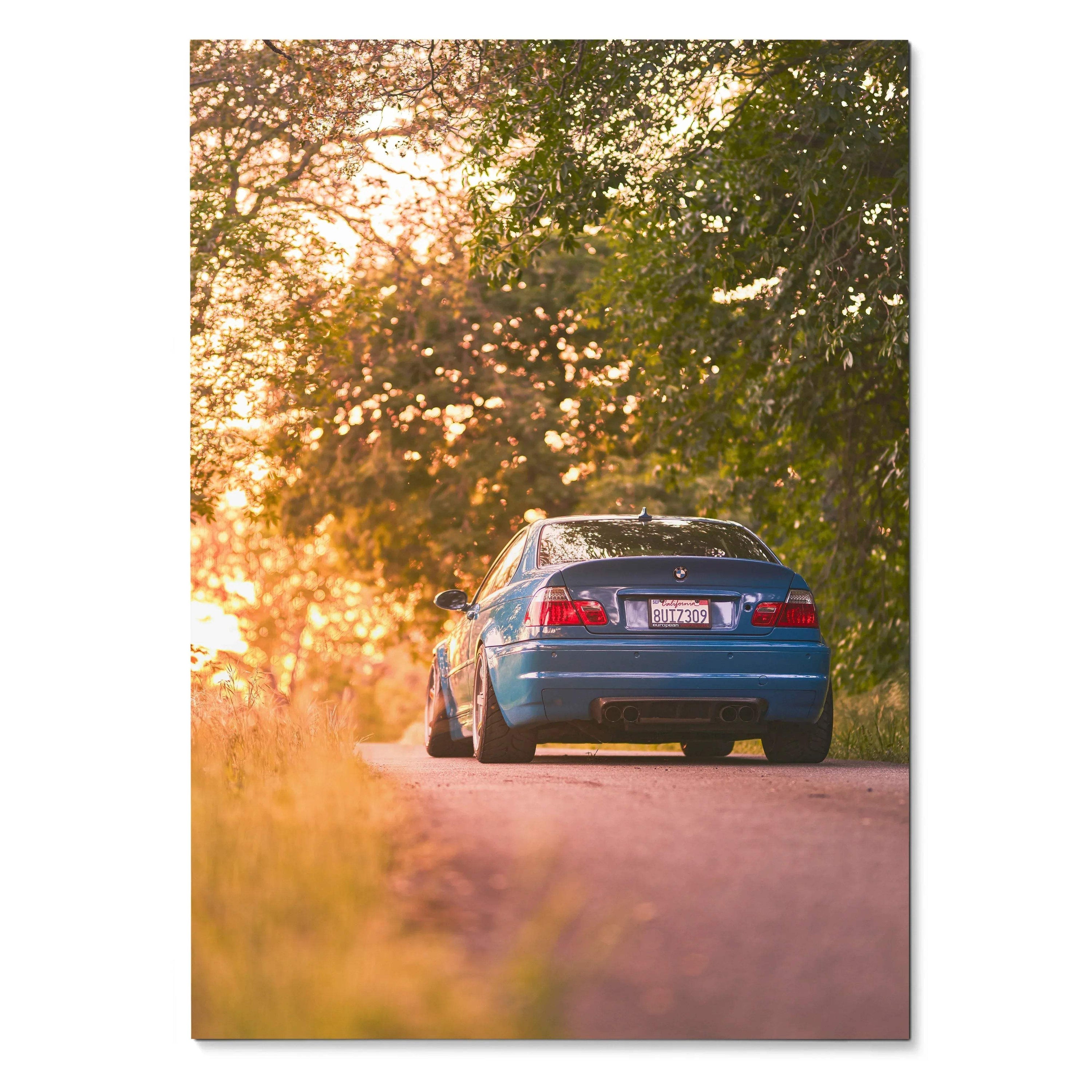 BMW E46 M3 poster showing rear view of blue car on sunset-lit road with trees, wall art decor.