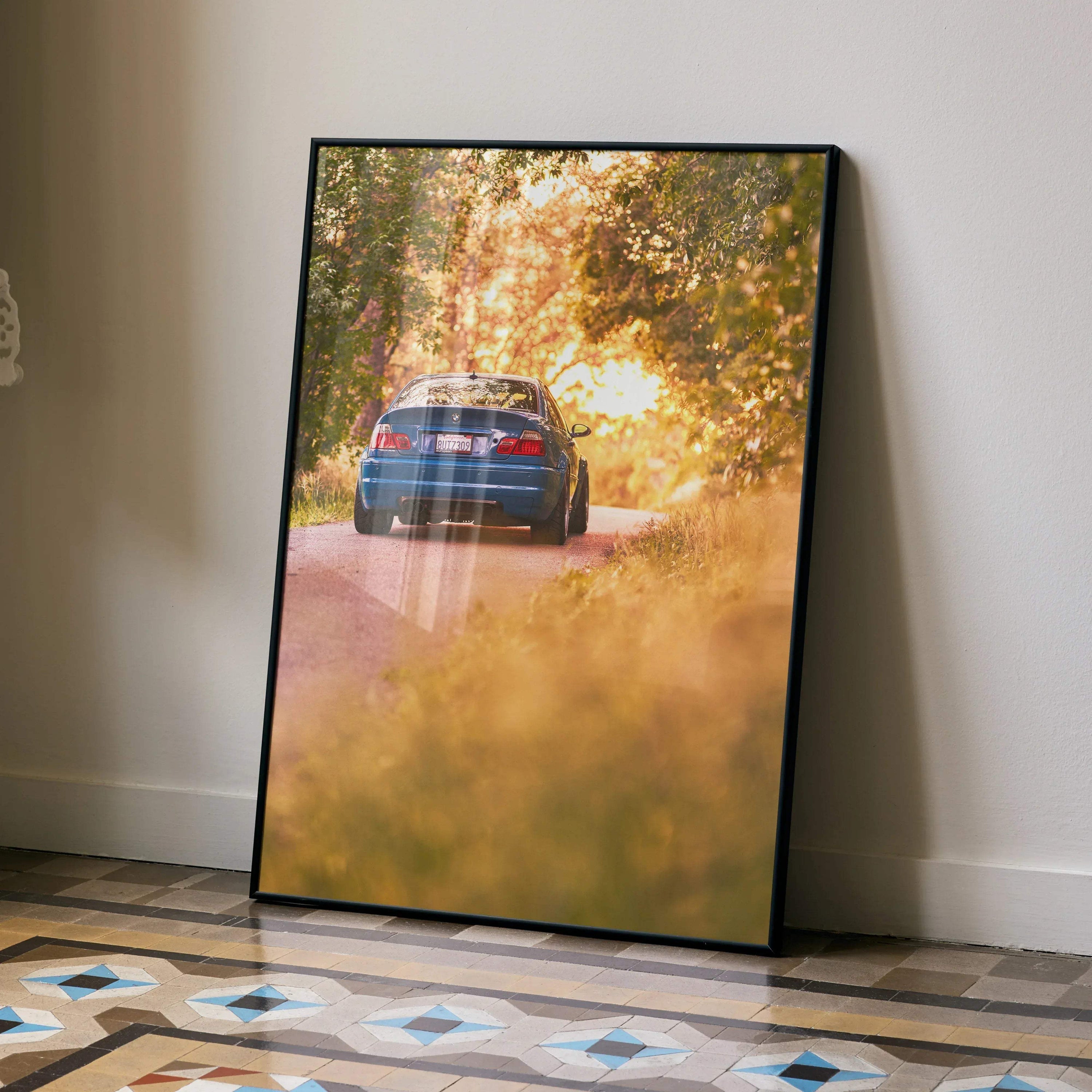 BMW E46 M3 driving on tree-lined road at sunset poster wall art with warm golden tones.