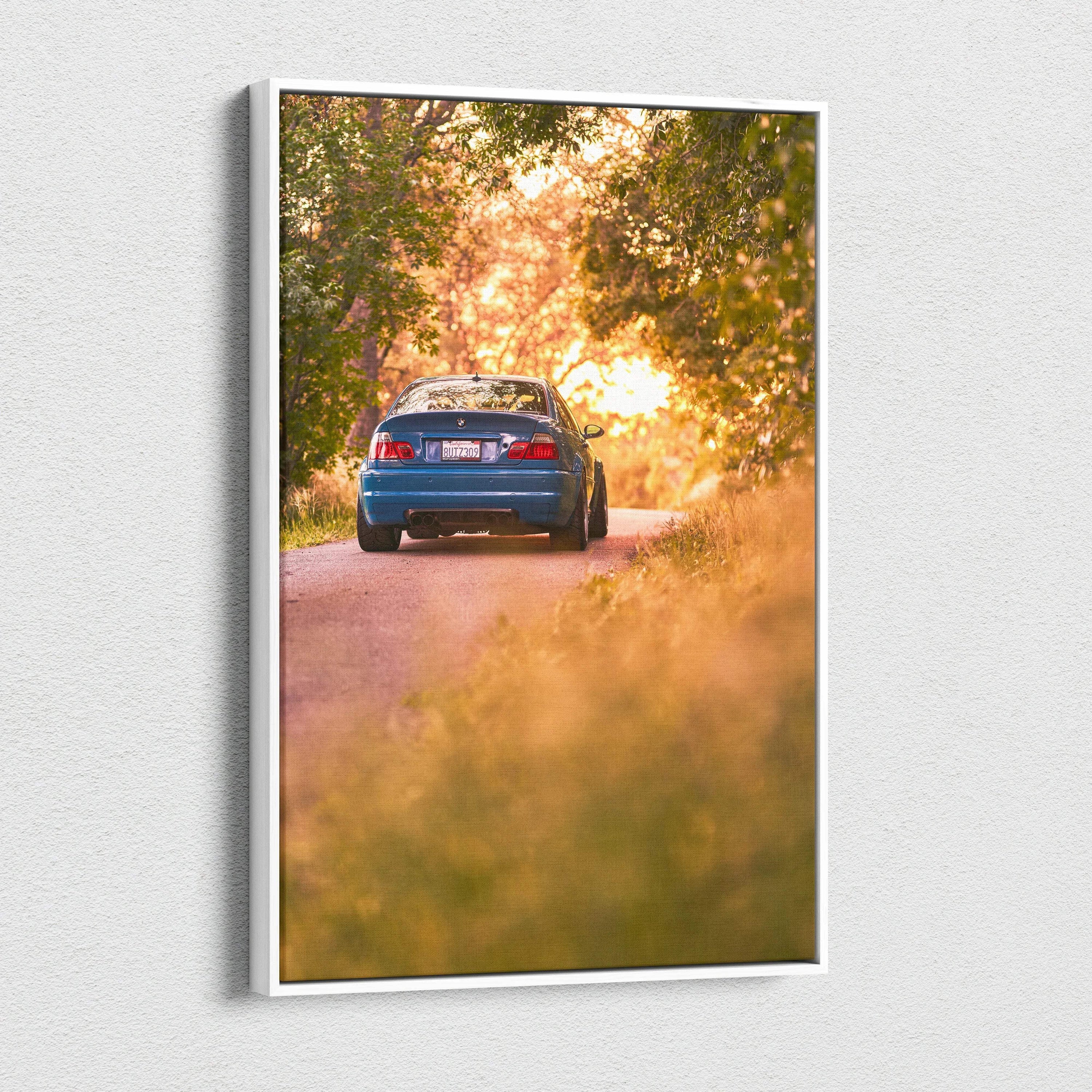 BMW E46 M3 driving on sunlit forest road canvas wall art with warm sunset colors.
