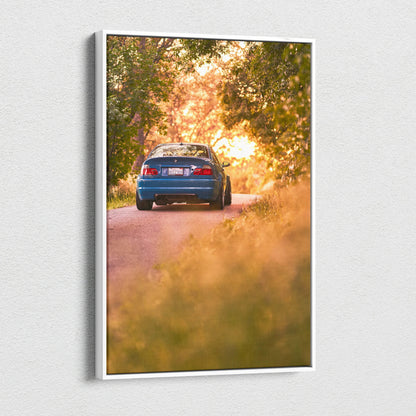 BMW E46 M3 driving on sunlit forest road canvas wall art with warm sunset colors.