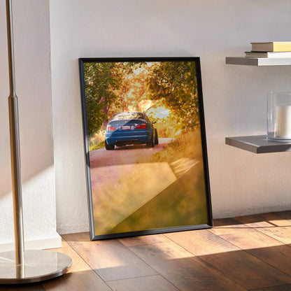 BMW E46 M3 driving into a sunlit autumn landscape poster wall art in black frame.