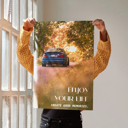 Motivational poster wall art featuring blue BMW E46 M3 on sunlit road with inspiring text "Enjoy Your Life Create Good.