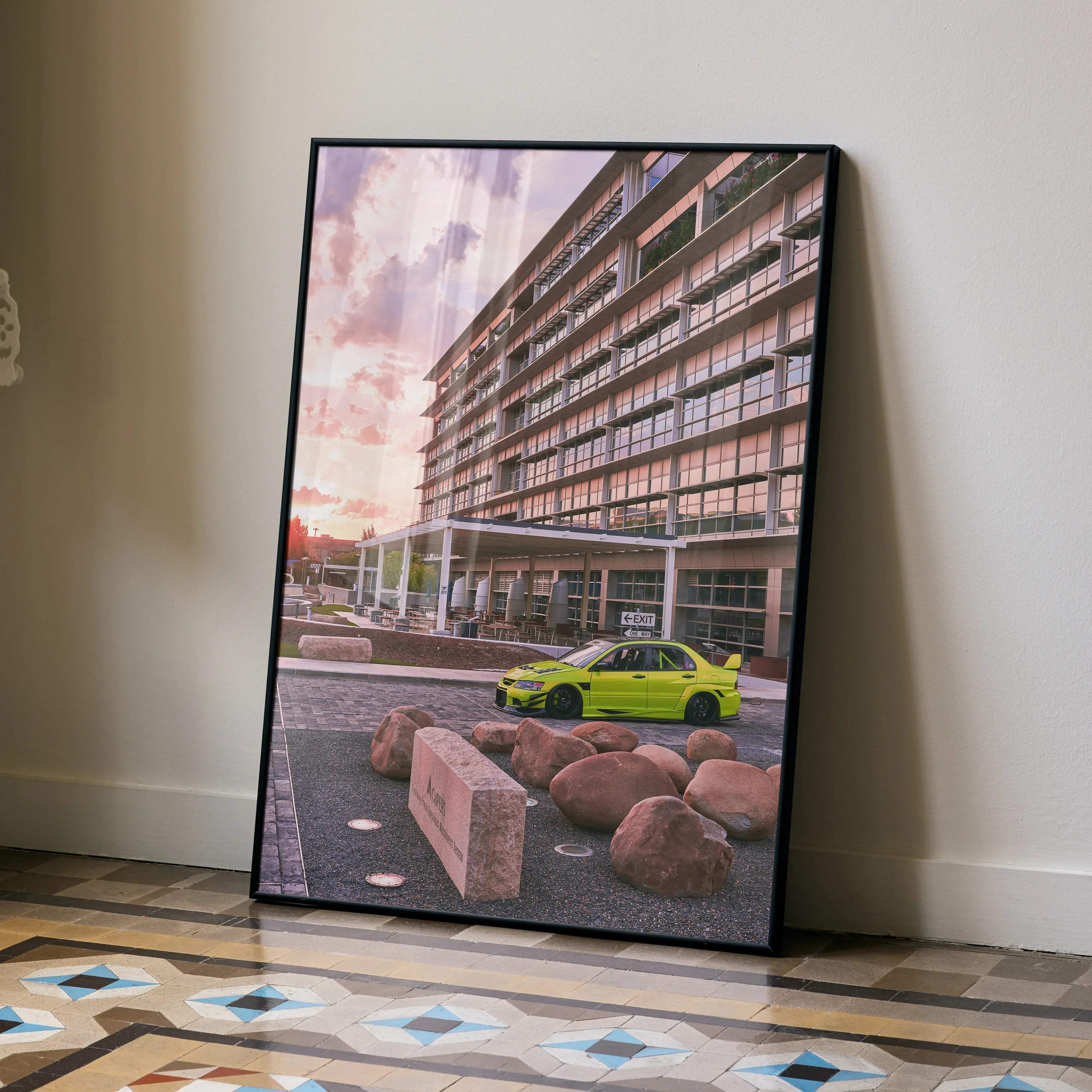 Black-framed canvas print of lime green mitsubishi evo 9 parked before modern building with pink sunset skies