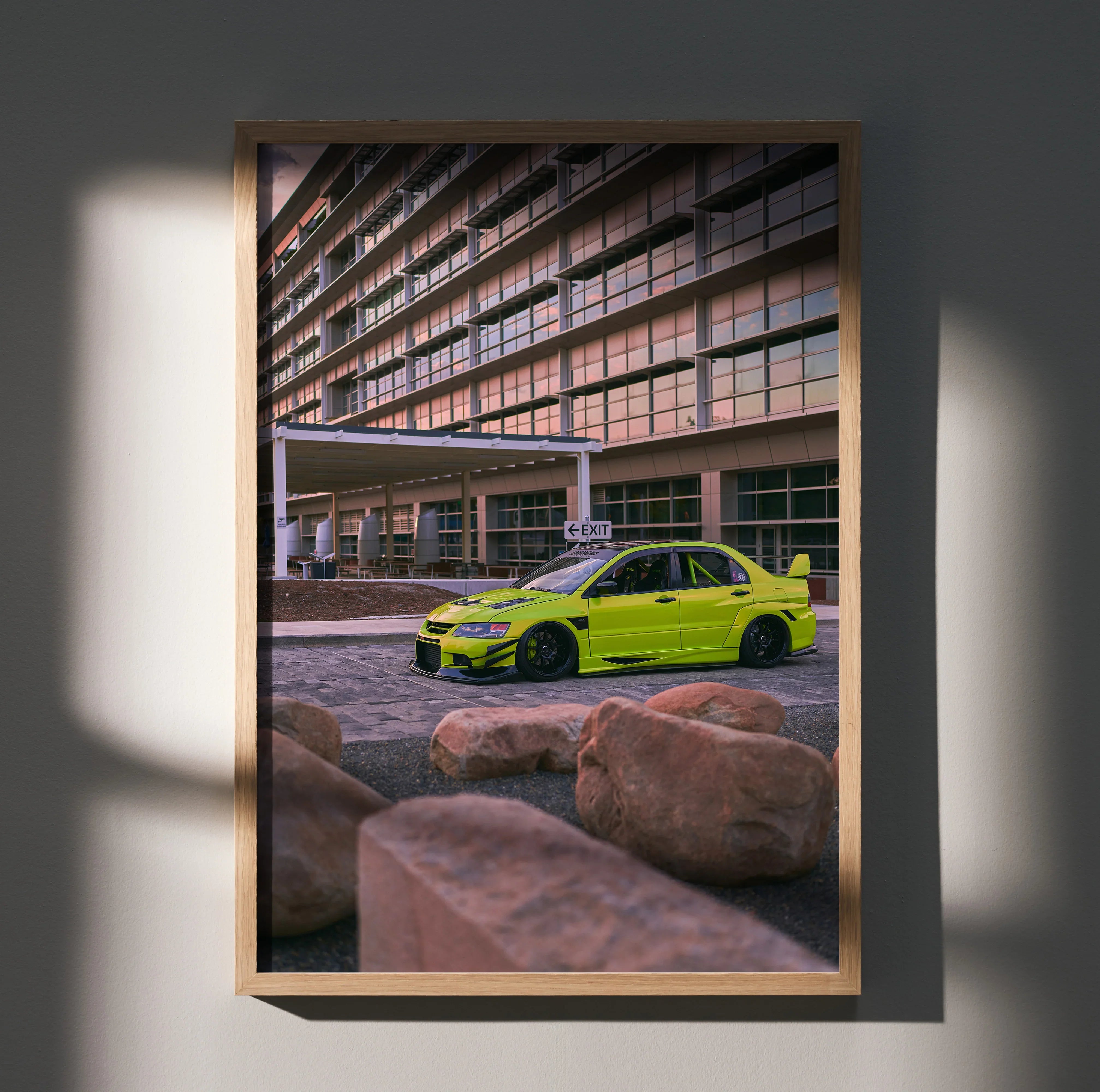 Mitsubishi Evo 9 in bright yellow parked by modern building poster wall art in wooden frame.